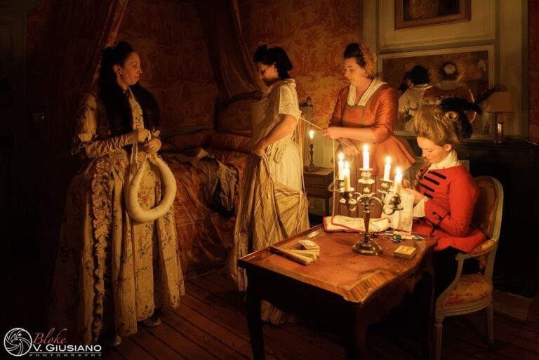 Figurantes costumées autour d’une table éclairée par un chandelier