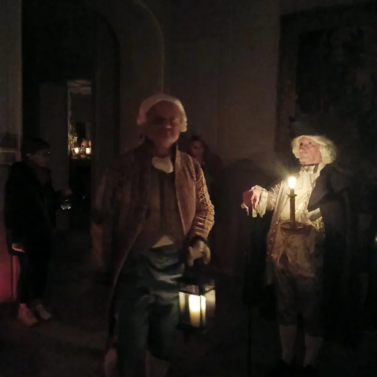 Figurants costumés dans une pièce sombre, une lanterne à la main