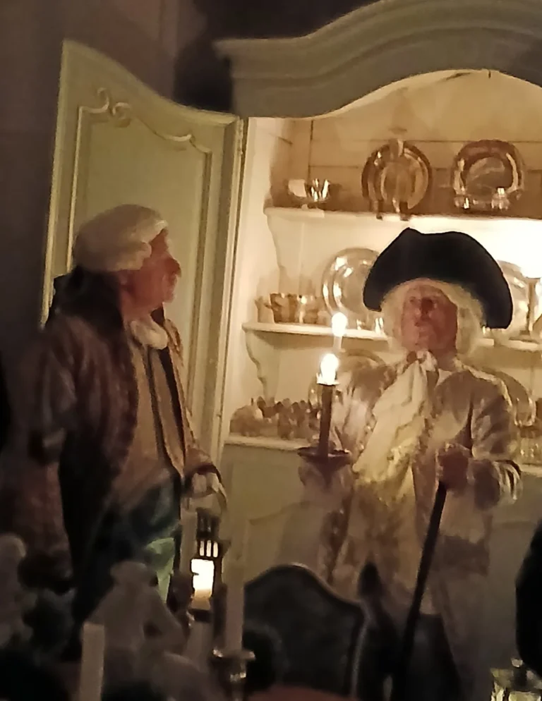 Figurants costumés devant un vaisselier, à la lueur d'une bougie